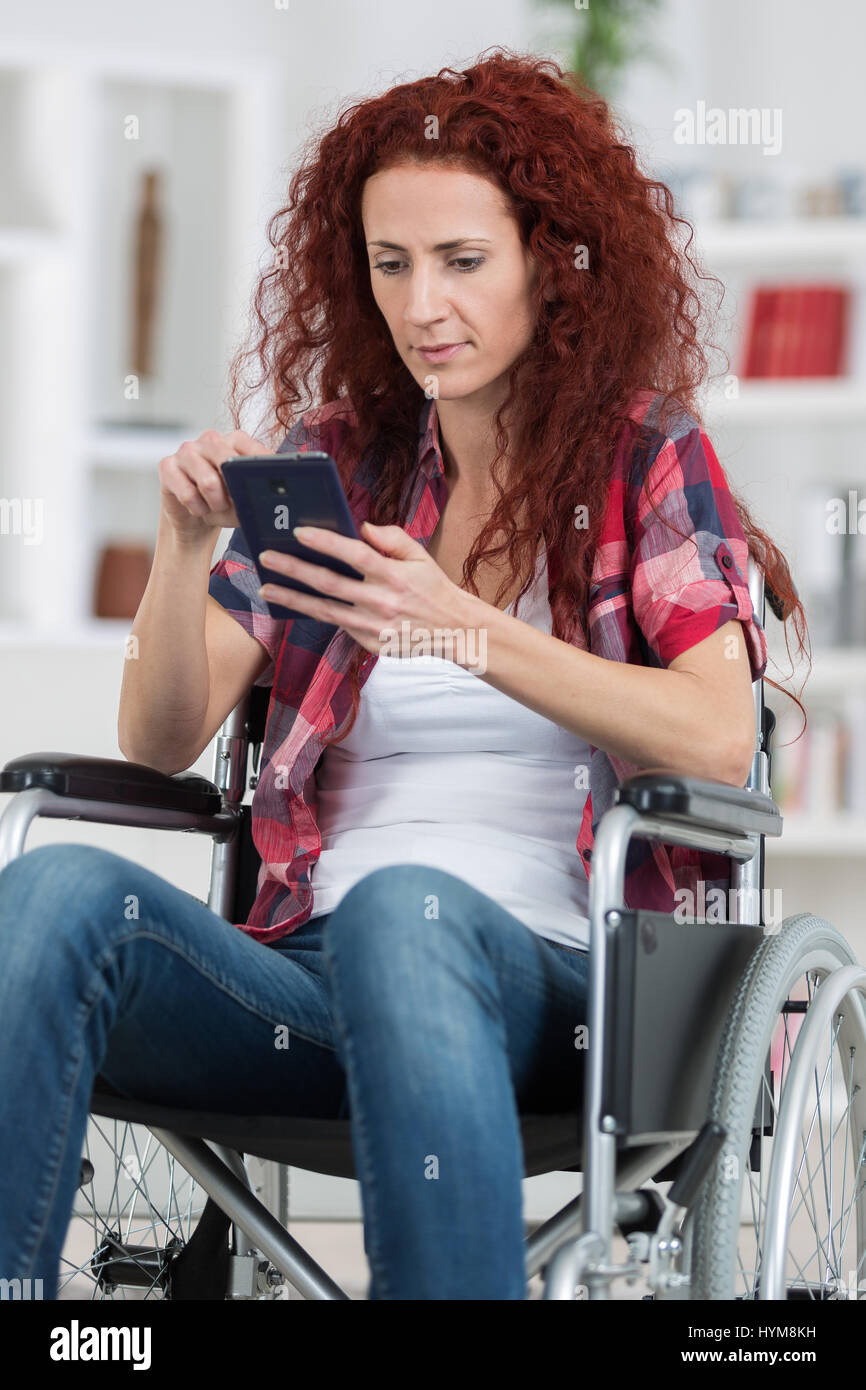 Donna disabile sedia a rotelle e digitando messaggio con lo smartphone Foto Stock