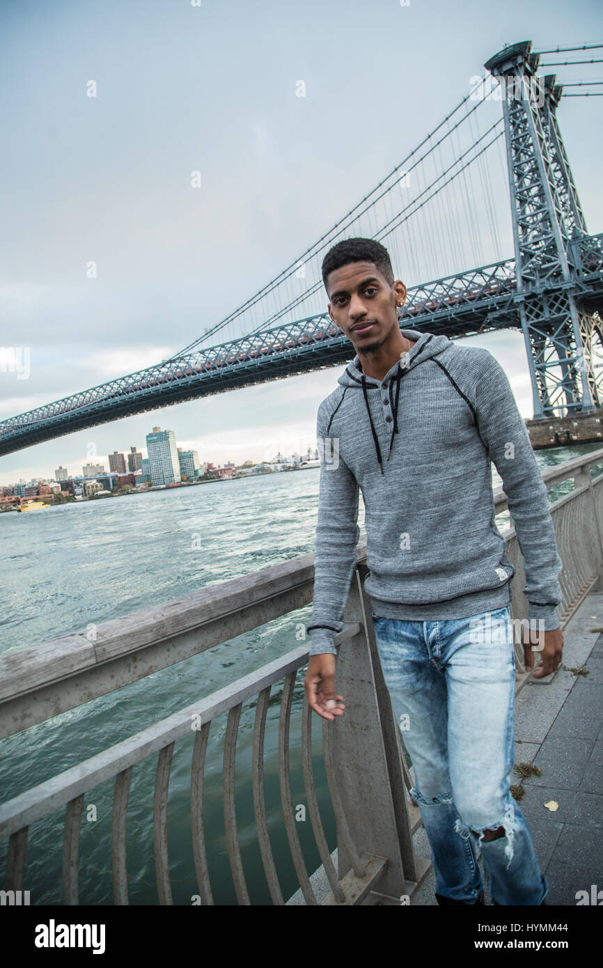 Un giovane uomo si siede e ammira la vista di NYC Williamsburg Bridge. Girato durante l'autunno del 2016 a Brooklyn, New York City. Foto Stock