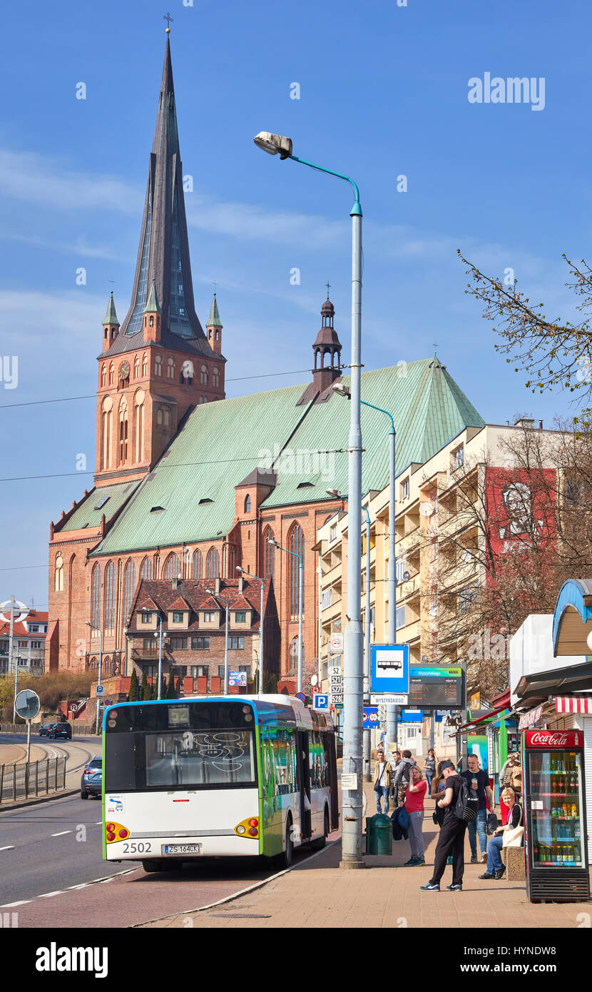Szczecin, Polonia - 01 Aprile 2017: Fermata Bus con persone in attesa a Wyszynskiego street, Basilica Cattedrale di San Giacomo Apostolo in background. Foto Stock
