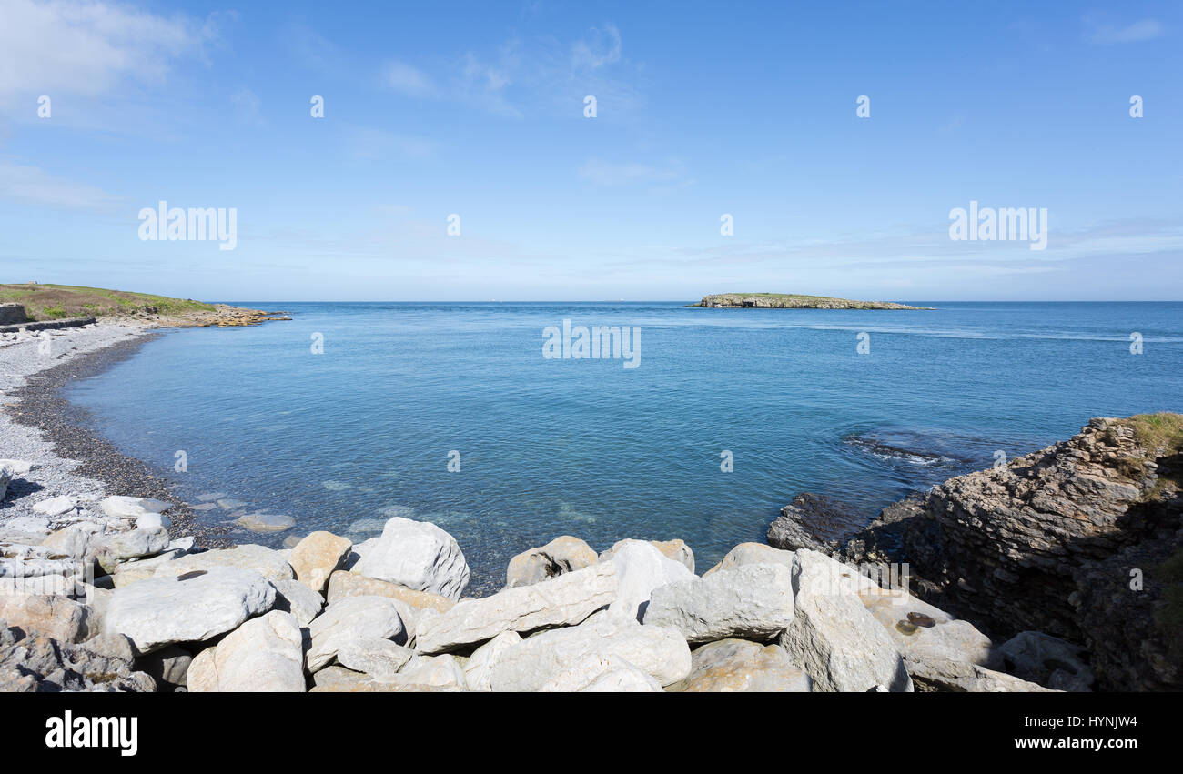 Coste rocciose a Moelfre, Anglesey nel Galles del Nord con vista in lontananza Moelfre Isola (Ynys Moelfre) Foto Stock