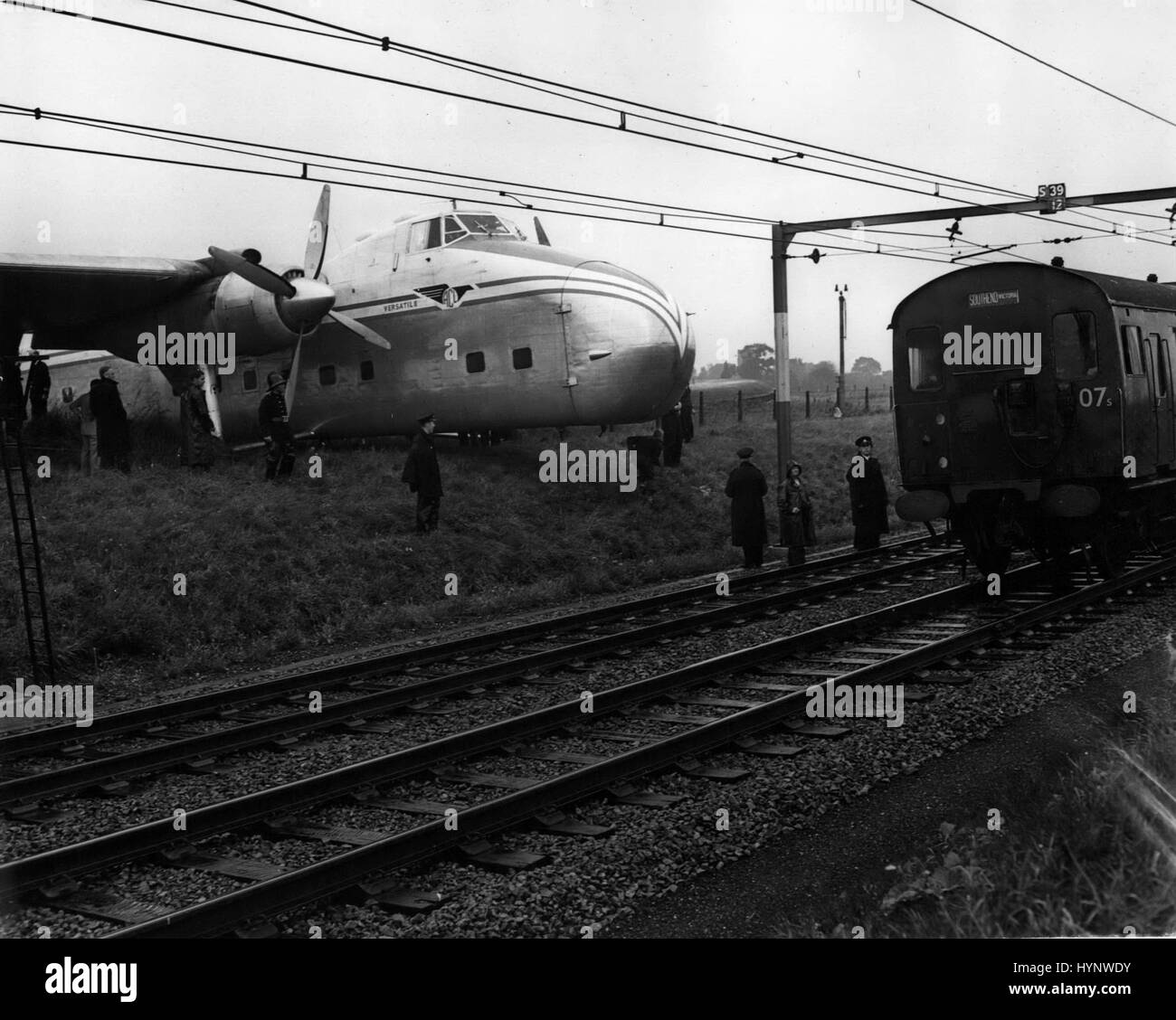 Agosto 08, 1957 - Piano va fuori pista - alle ferrovie. Crash vicino a Southend: Tredici persone hanno avuto la fortuna di un fuga di ieri quando un passeggero-freighter aeromobile in cui esse sono state viaggiando crash-sbarcati a Rochford, Essex. Esso skidded sulla pista in atterraggio a aeroporto di Southend da Calais, arata attraverso una recinzione perimetrale e arrestato sulla diga ferroviaria. Il velivolo, un Bristol freighter portante era tre vetture come pure i tre uomini di equipaggio e dieci passeggeri. Mostra fotografica di treni continuano il loro viaggio che mostra l'aereo si è schiantato a lato della pista a Rochford, Essex, Foto Stock