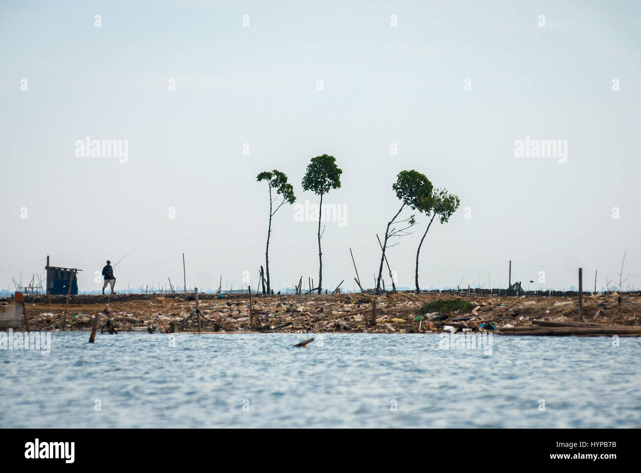 Un pescatore che cammina su una terra bonificata sull'estuario del canale delle inondazioni di Giacarta, sul confine provinciale tra Giava Occidentale e Giacarta, Indonesia. Foto Stock