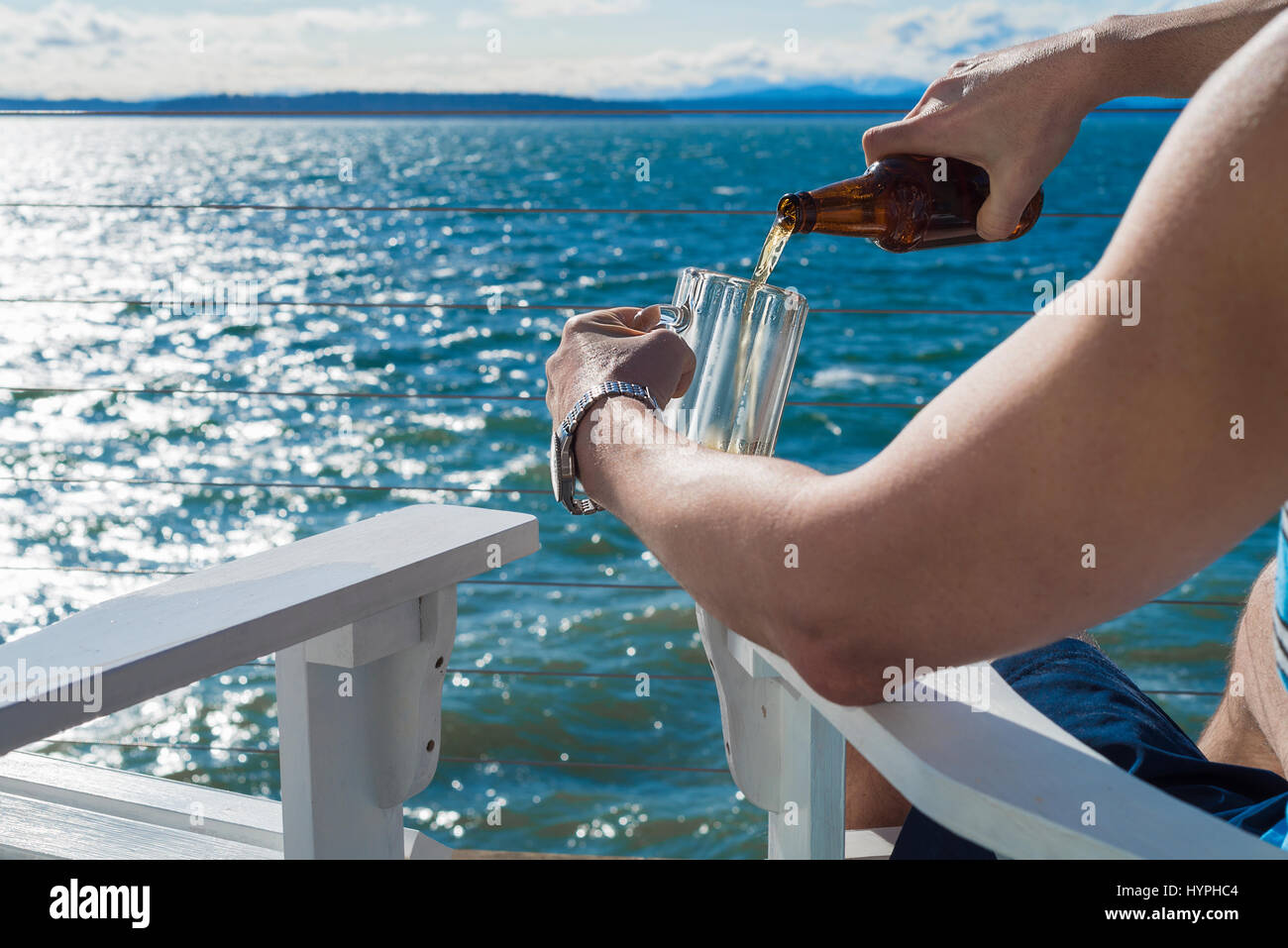 Uomo seduto sul mare microbrew versatore in frosty mug seduti nelle sedie di adirondack Foto Stock