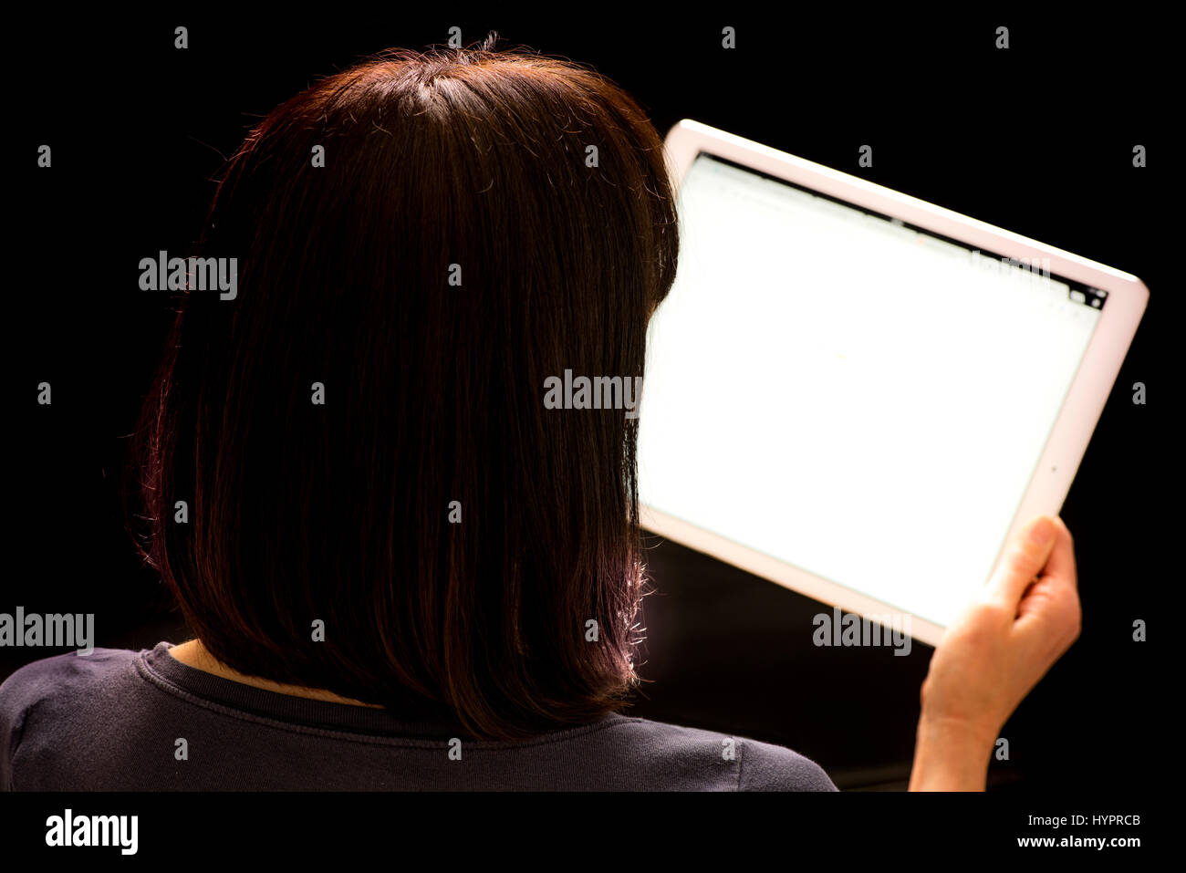 Donna che guarda l'iPad Pro tenuto in mano contro lo sfondo nero Foto Stock
