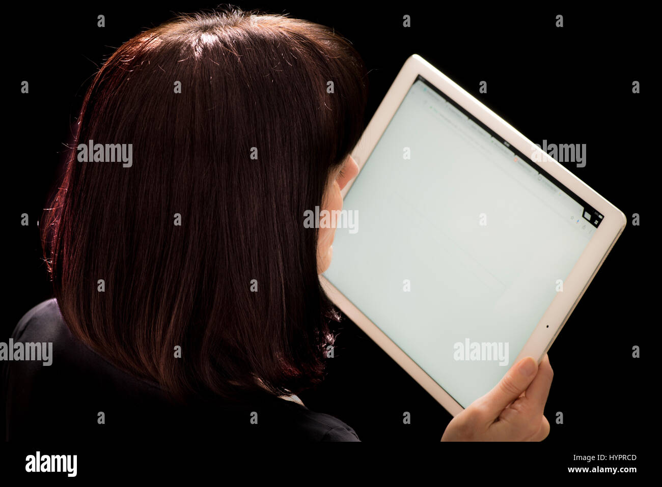 Donna che guarda l'iPad Pro tenuto in mano contro lo sfondo nero Foto Stock