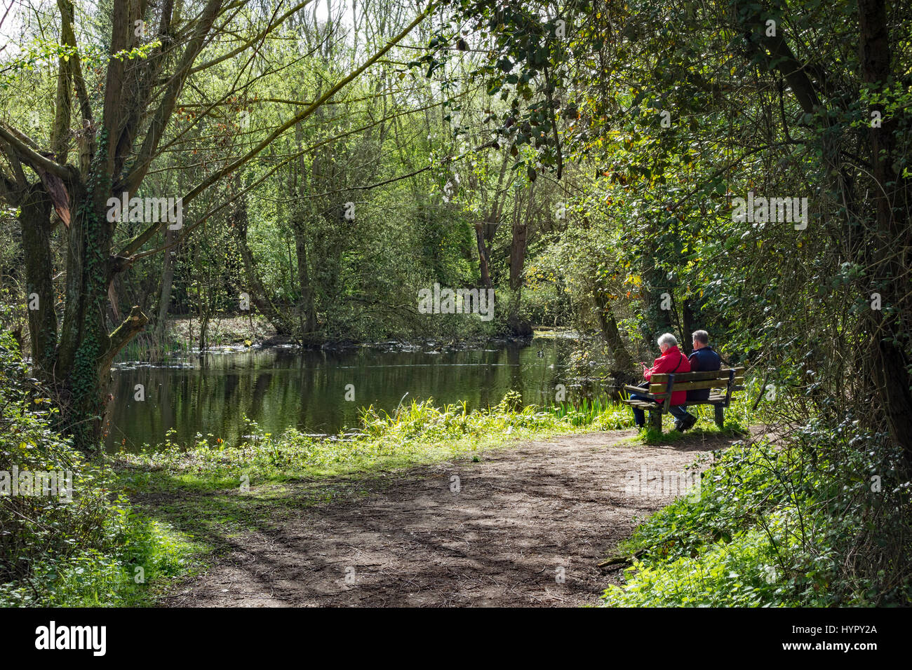 Coppia di anziani seduti su un banco di lavoro accanto al lago godendo di sole di primavera Foto Stock