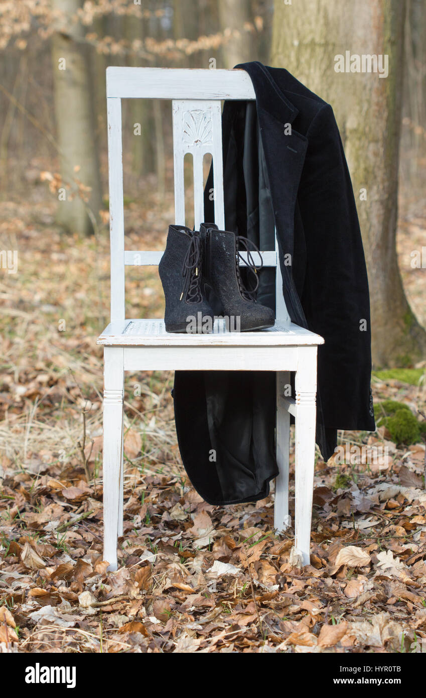 Una sedia bianca con nero scarpe a tacco e giacca nella foresta Foto Stock