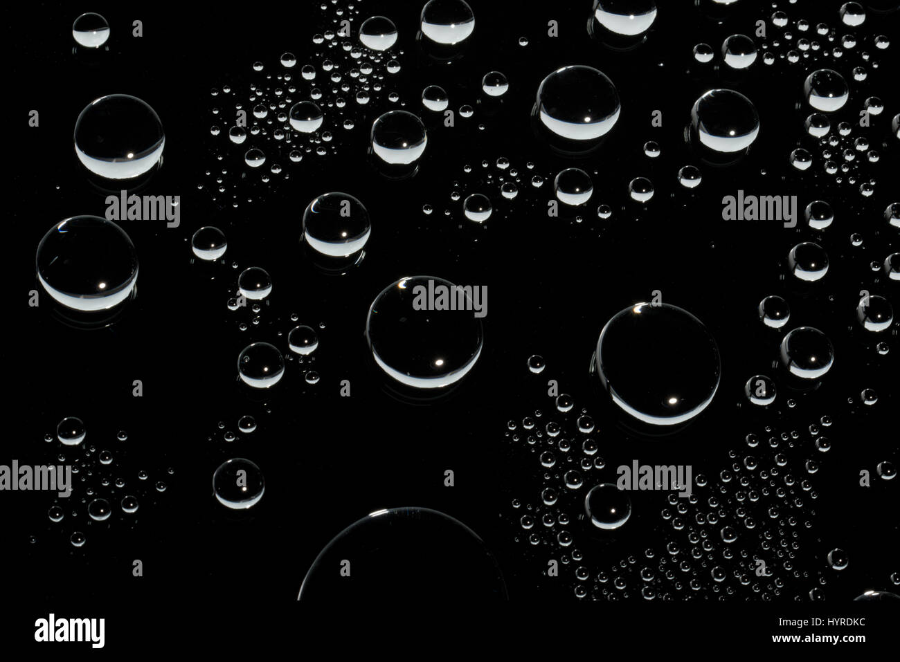 Una forma rotonda goccioline di acqua sulla superficie di vetro. Sfondo scuro dietro. Foto Stock