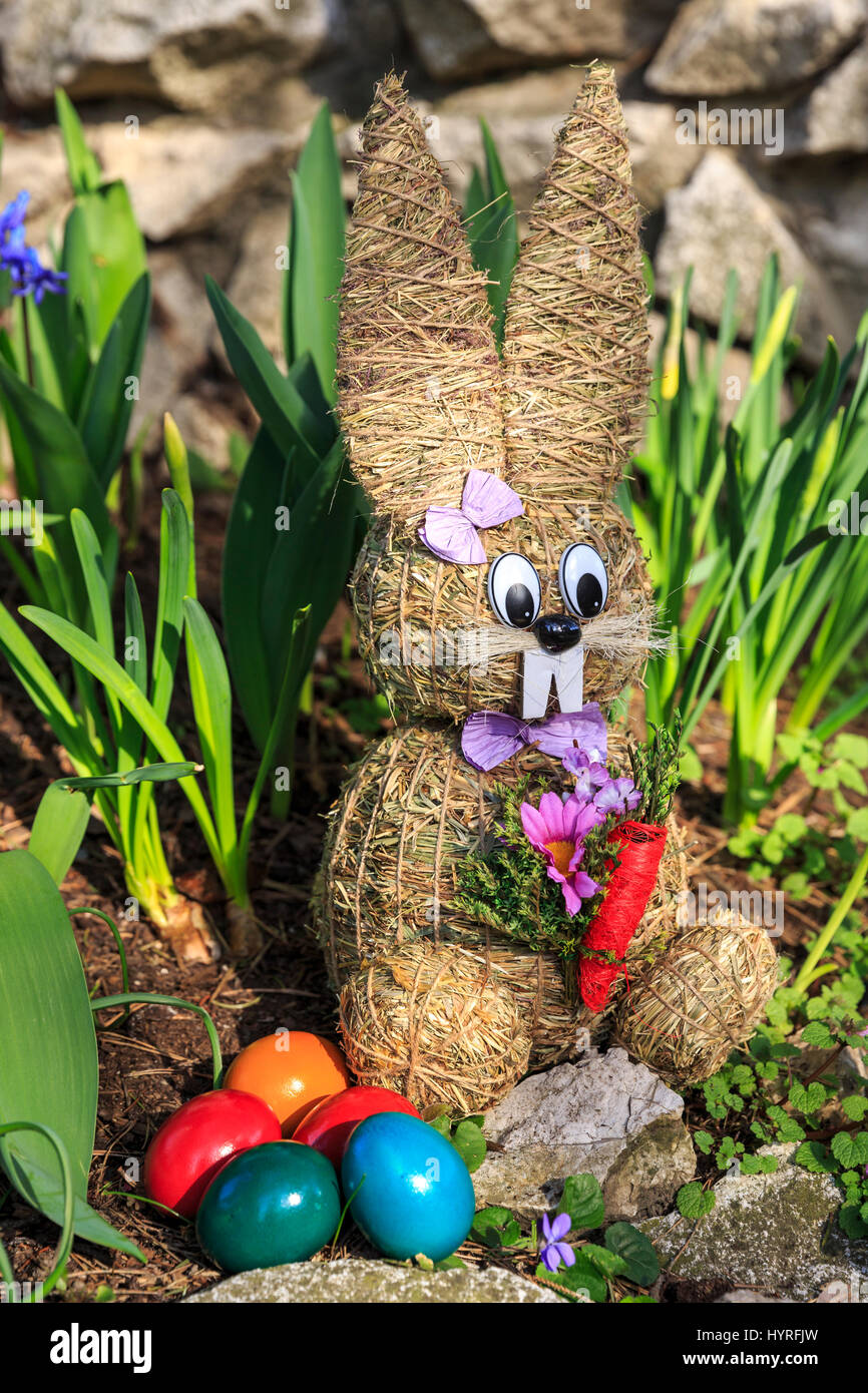 Coniglietto di pasqua fatta di paglia e tinte colorate uova di pasqua nel letto di fiori Foto Stock