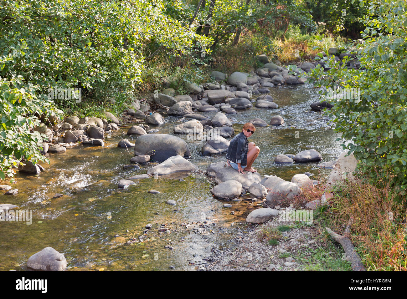 Conciato al bianco donna di mezza età seduta sulla roccia di fiume di montagna Matekova in autunno. Carpazi ucraini, la regione Transcarpazia, Mukachevo Foto Stock