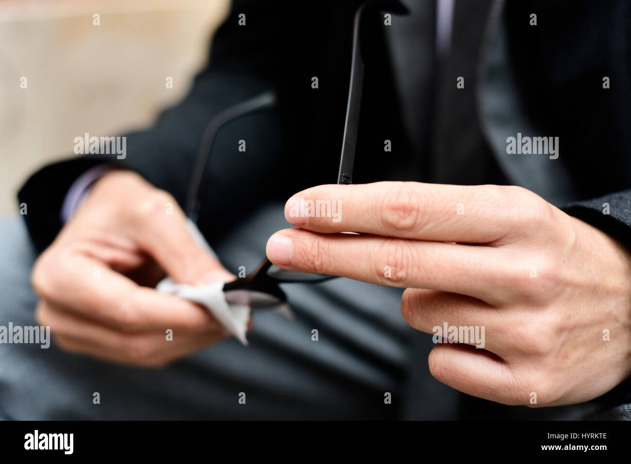 Primo piano di un giovane imprenditore caucasico in grigio di una tuta e un mantello nero pulizia delle lenti dei suoi occhiali con un panno in microfibra all'aperto Foto Stock