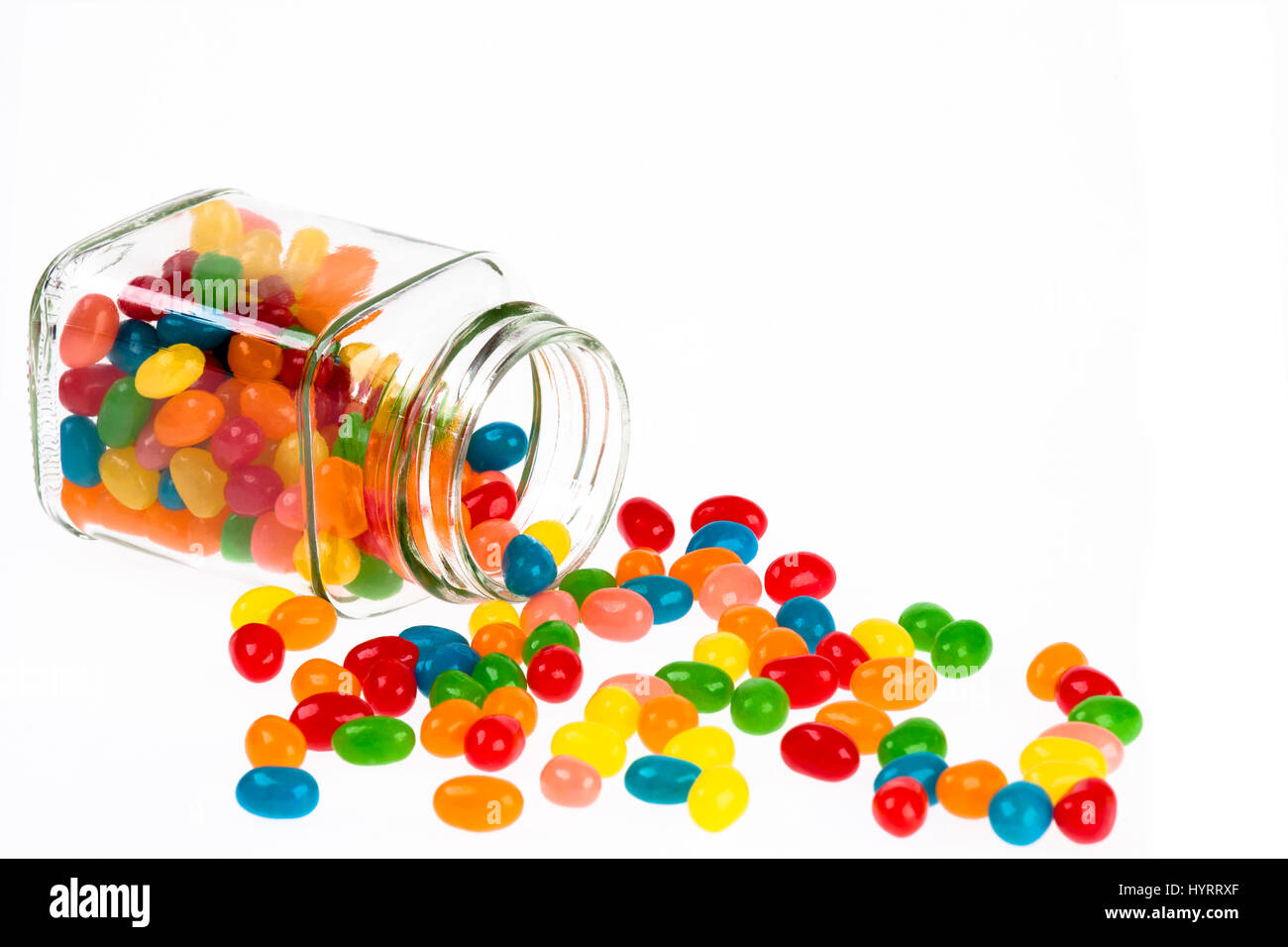 Primo piano di un delizioso Jelly Beans candy versato da un barattolo di vetro isolato su uno sfondo bianco Foto Stock