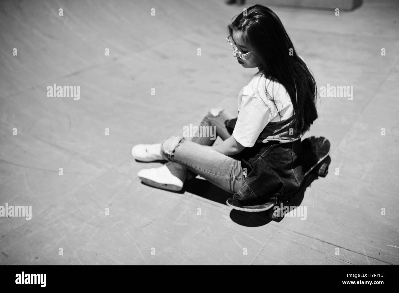 I giovani adolescenti ragazza urbano con lo skateboard, usura sui bicchieri, cappuccio e jeans strappati a skate park la sera. Foto Stock