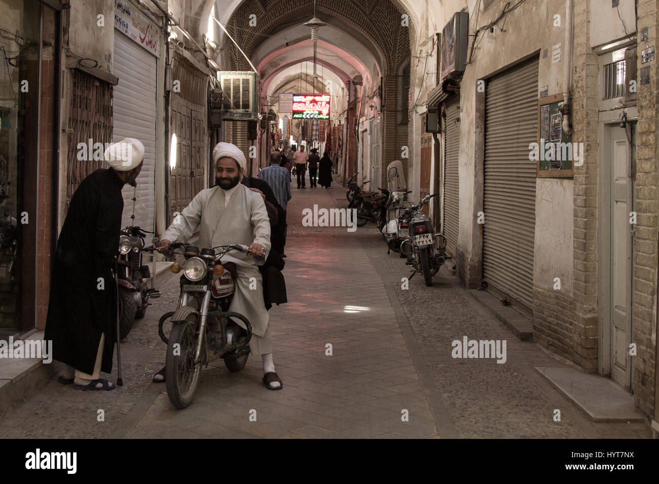 Yazd, Iran - agosto 18, 2016: imam iraniano indossando abiti tradizionali discutendo mentre su una moto in una strada coperta di yazd bazaar di immagine Foto Stock