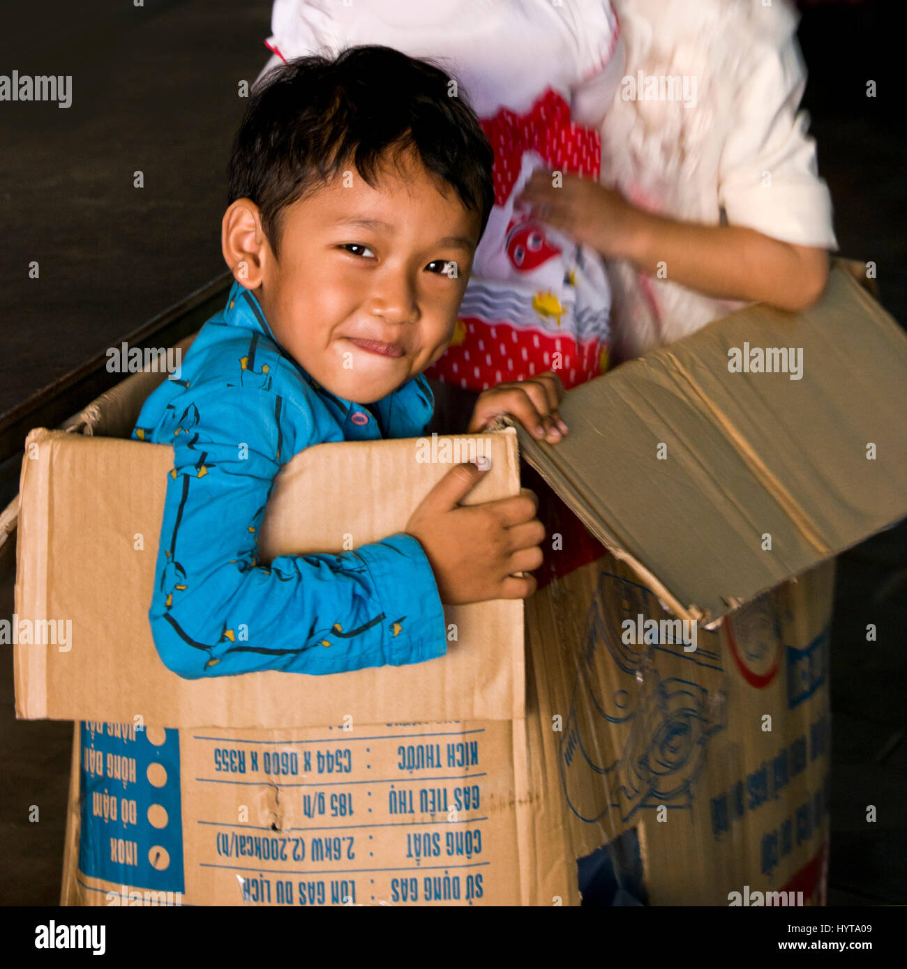 Square ritratto di una giovane ragazzo giocando all'interno di una scatola di cartone in Cambogia. Foto Stock