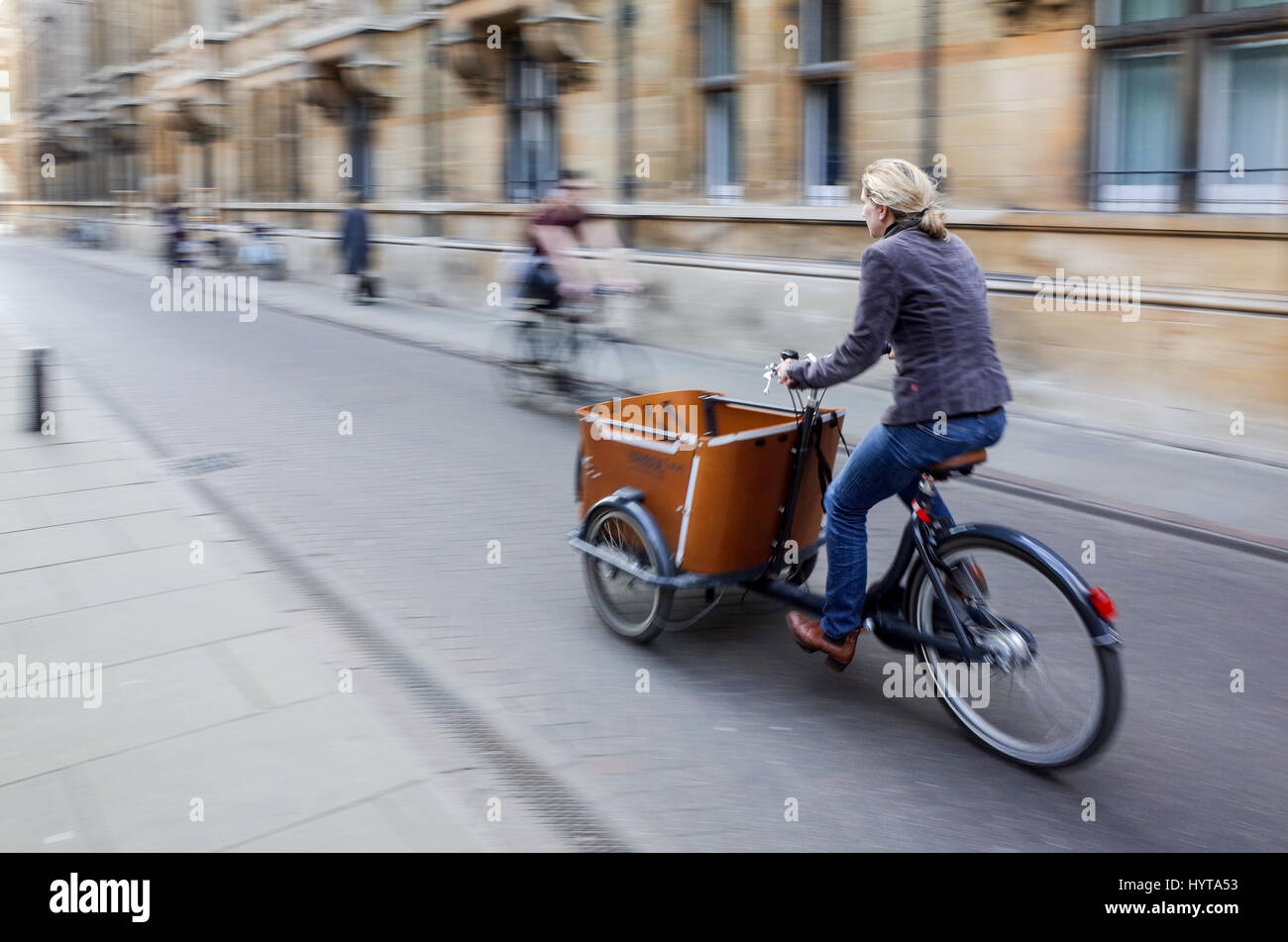 Una donna che cavalca un cargo in bicicletta attraverso le strade del centro di Cambridge, Regno Unito Foto Stock