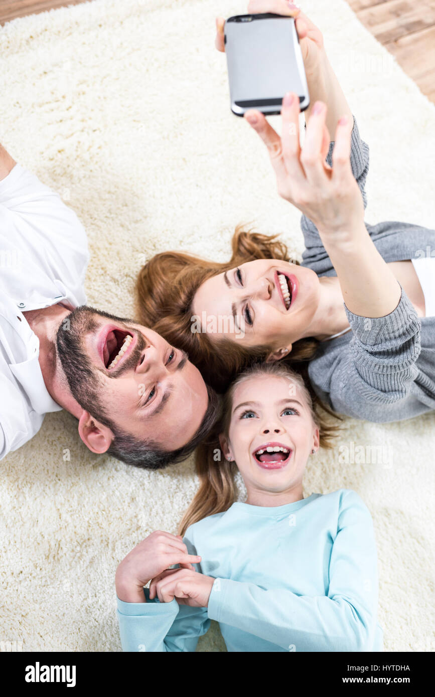 Vista superiore della famiglia giovane rendendo selfie sdraiati su un tappeto Foto Stock