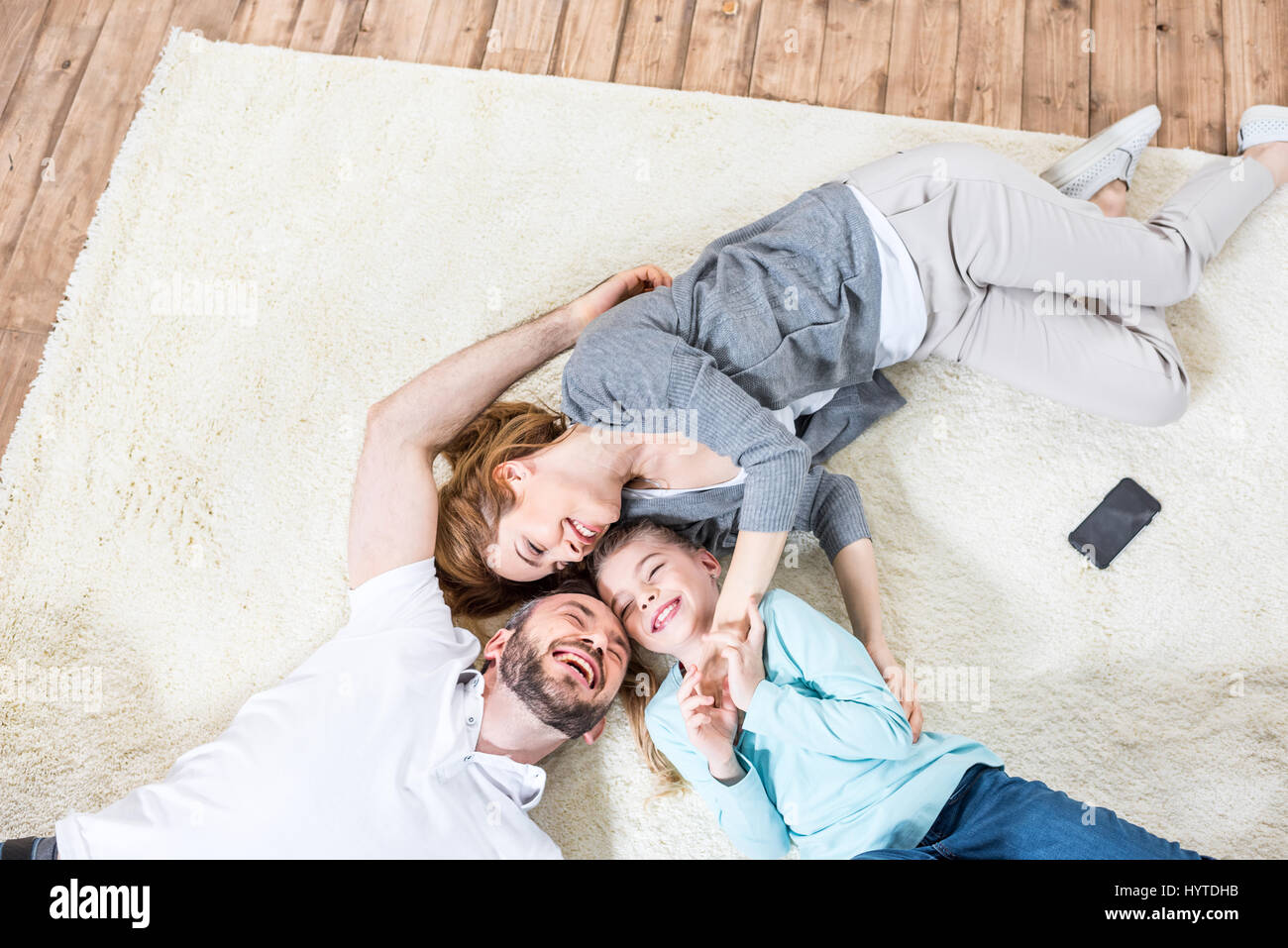 Vista superiore della famiglia di tre persone in un momento di relax a casa sdraiato sul tappeto e ridere Foto Stock