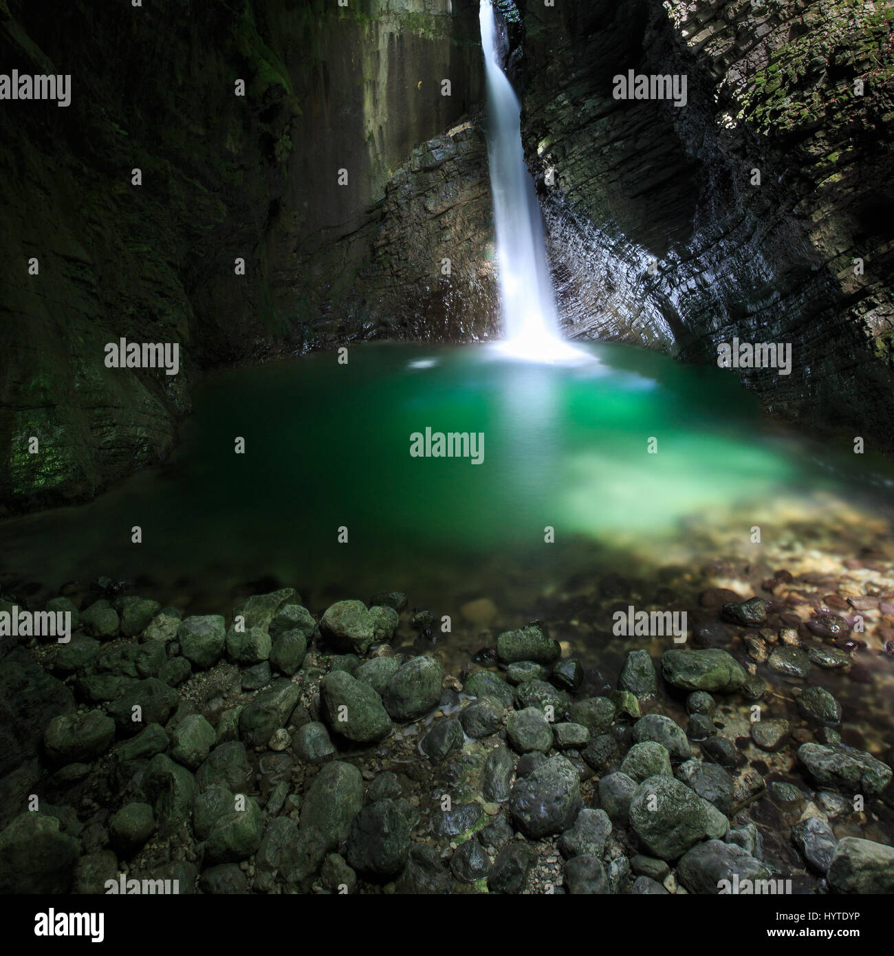 Romantica nascosta una cascata che scorre attraverso un crepaccio, cadendo in profondità in una stretta gola, formando il lago verde, illuminata da strette sunray, penetrare all'c Foto Stock