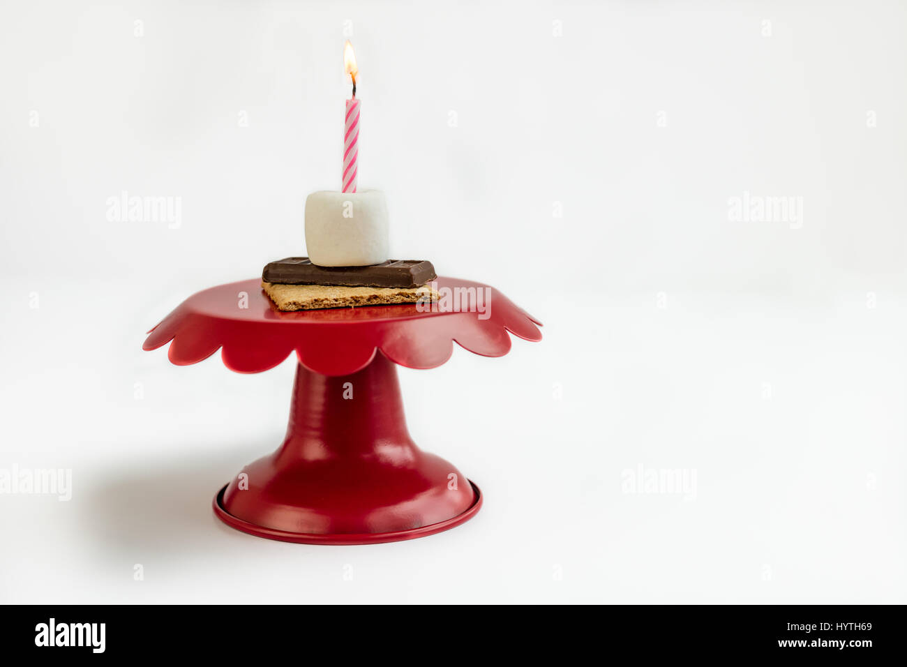S'more sorpresa di compleanno sulla torta rossa piastra con una rosa e bianco candela accesa per festeggiare il compleanno mangiando marshmallow, cioccolato, e Graham cracker. Foto Stock