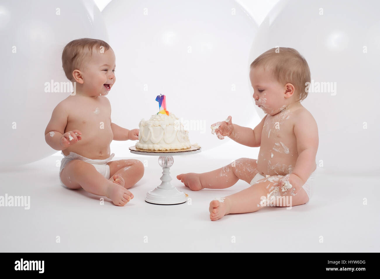 Un anno vecchio twin boys indossa pannolini e mangiare la torta di compleanno. Il detergente dei due sembra essere ridere a suo fratello disordinato. Foto Stock