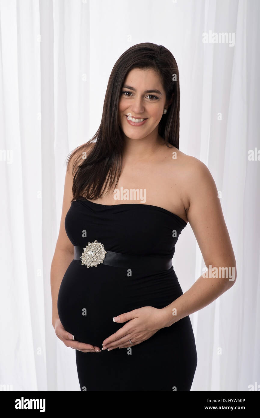 Ritratto di una bella donna incinta che indossa un nero, senza spalline, abito di maternità. Lei è sempre sorridente e guardando la telecamera. Foto Stock