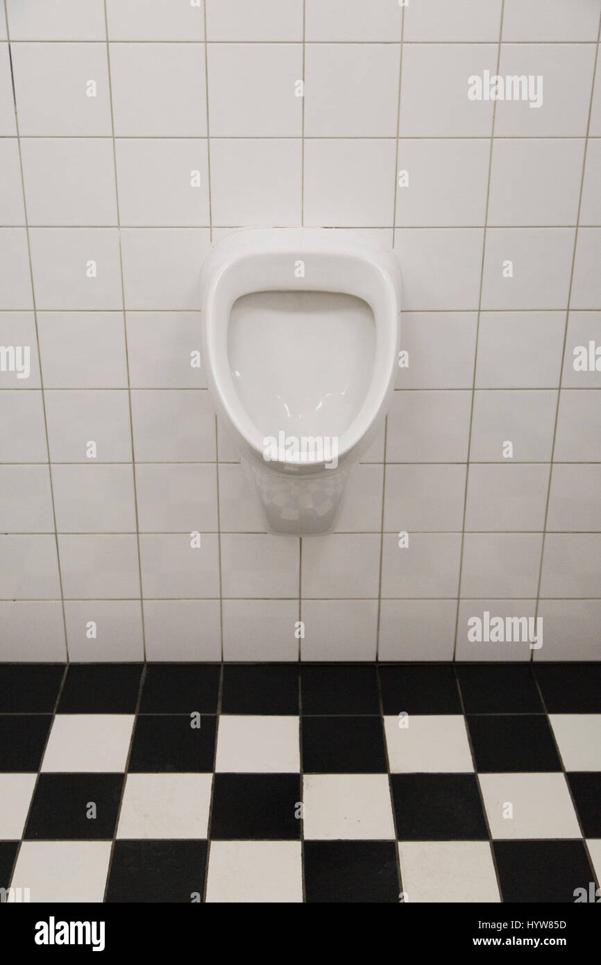 Un orinatoio in una toilette maschile. Il bagno è in bianco e nero controllato di piastrelle. Foto Stock