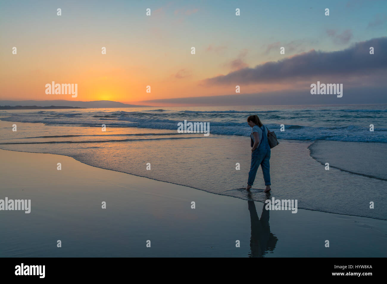 A piedi nudi donna camminare e pensare in mare durante il tramonto in spiaggia Foto Stock