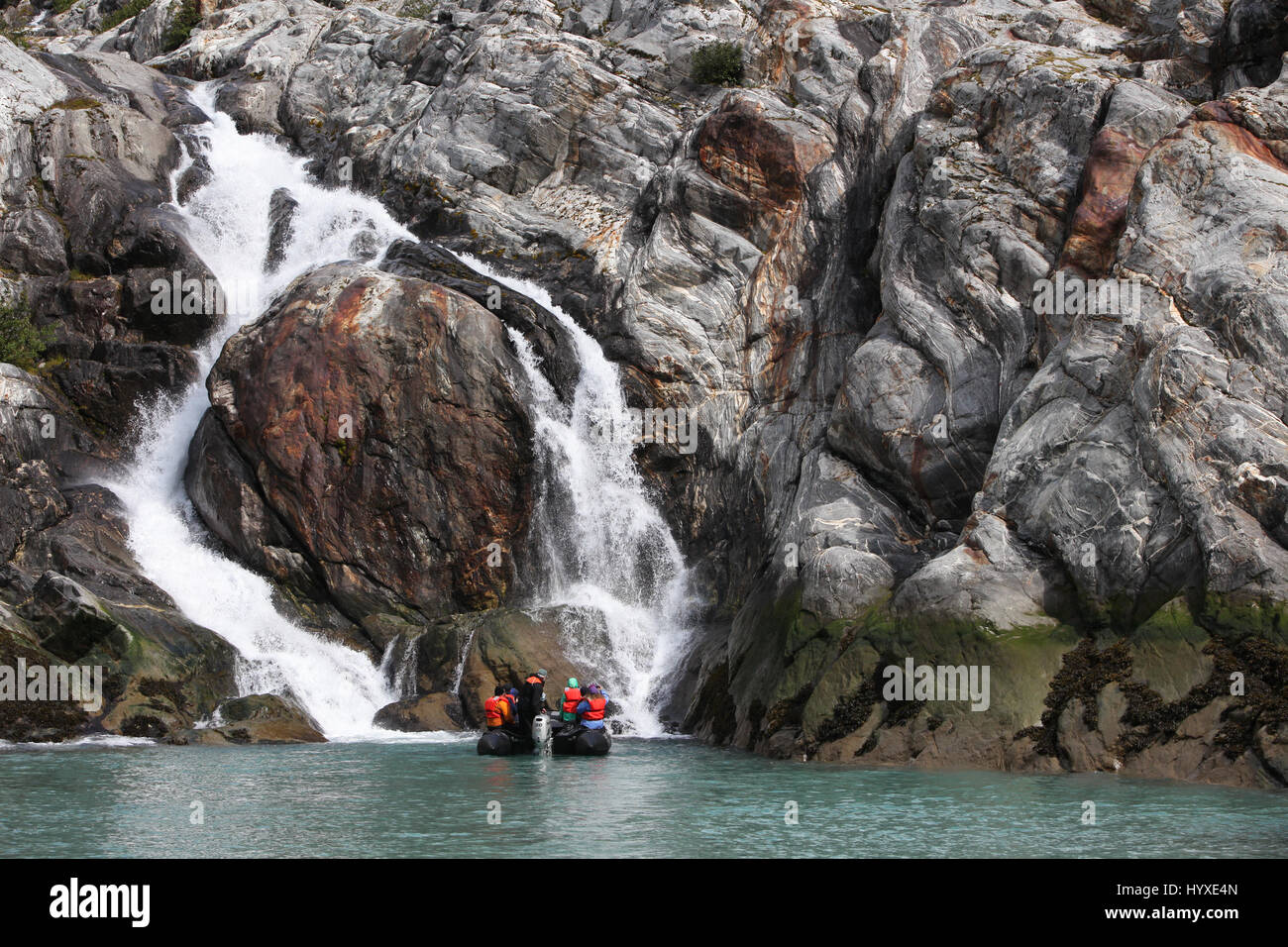 I viaggiatori in una barca Zodiak navigare nei pressi di una cascata che è stata formata dal ghiacciaio runoff. Foto Stock