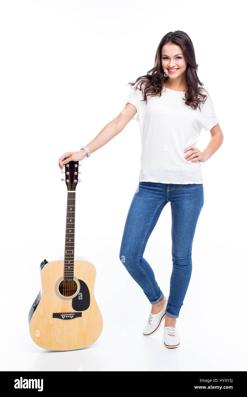 Bella giovane donna in piedi con la chitarra e sorridente in telecamera su bianco Foto Stock