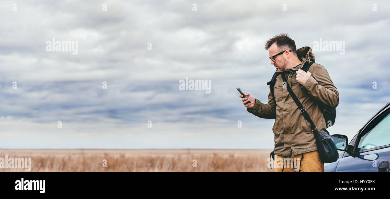 Escursionista in piedi nella prateria dalla vettura e utilizzo di smart phone Foto Stock