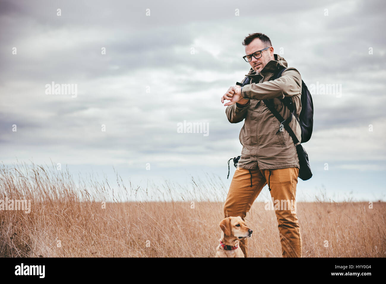 Escursionista con il cane in piedi nella prateria e guardando a guardare Foto Stock