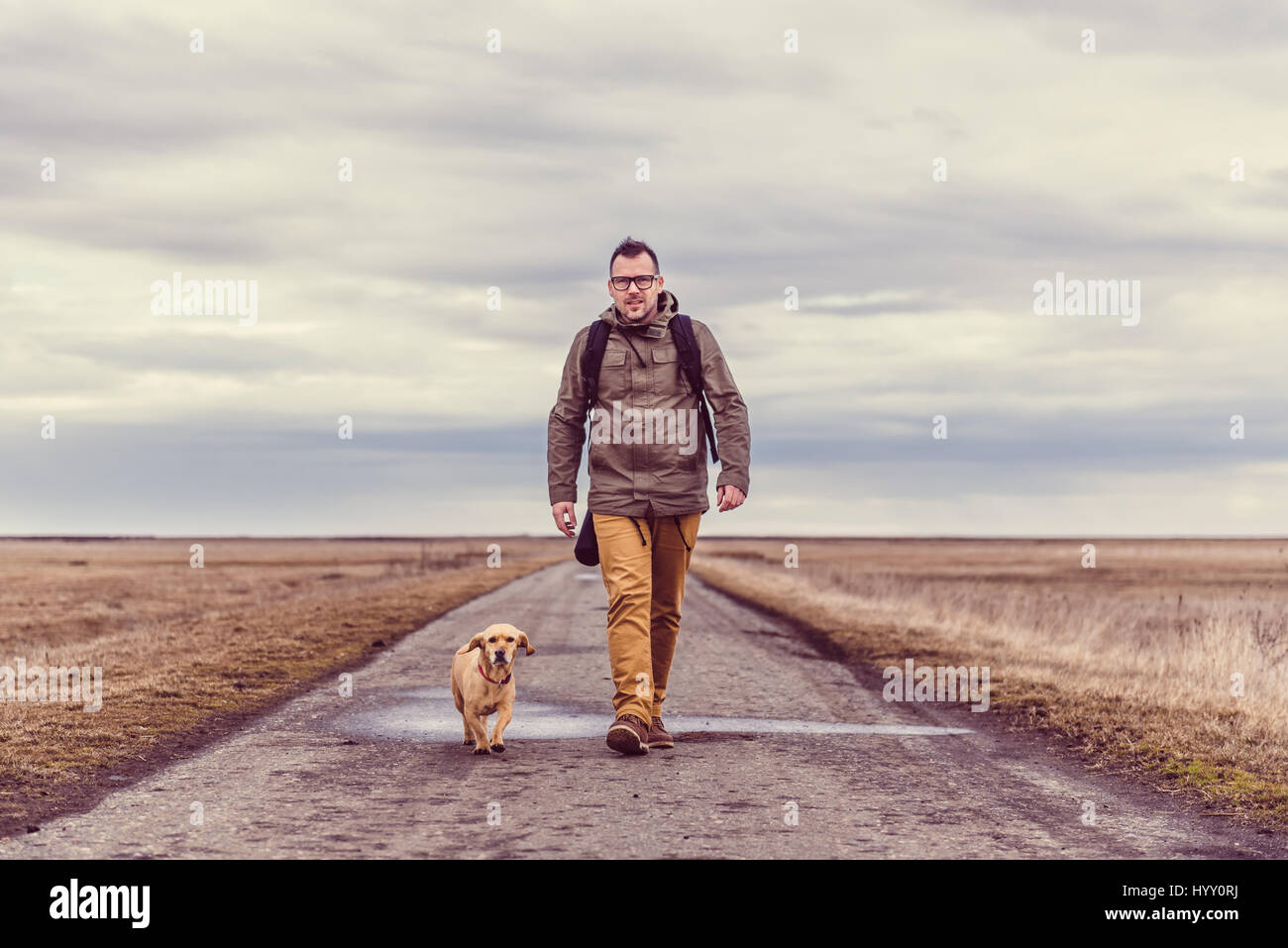 Escursionista e cane a camminare lungo una strada in un giorno nuvoloso Foto Stock