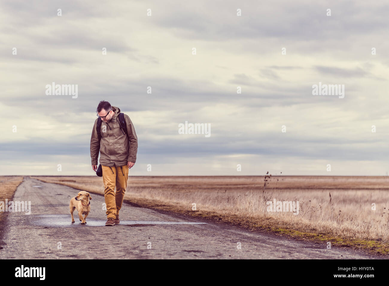 Escursionista e cane a camminare lungo una strada in un giorno nuvoloso Foto Stock