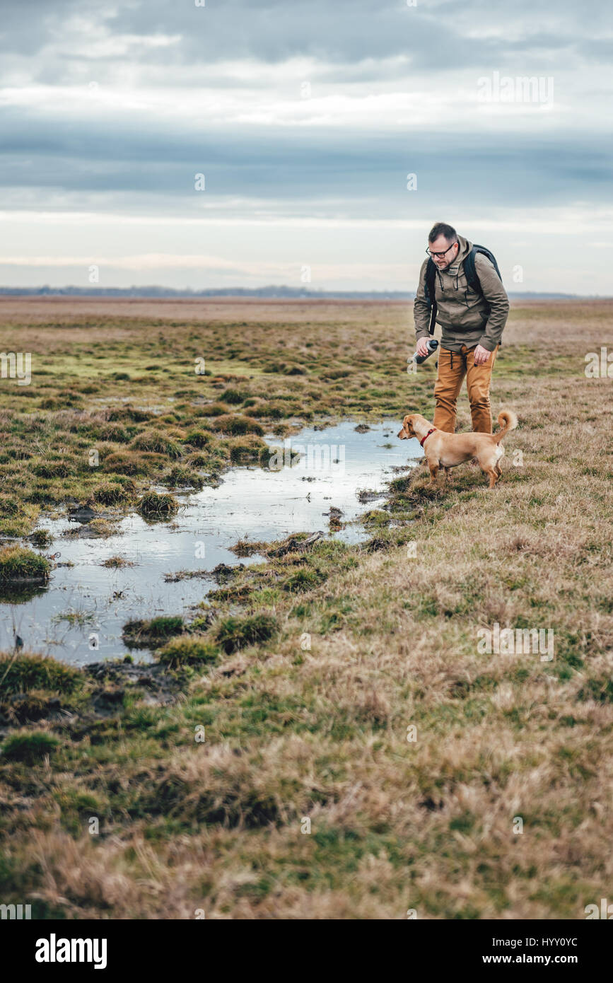 Escursionista e cane da lo stagno in prati in un giorno nuvoloso Foto Stock