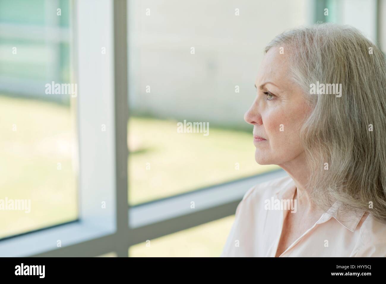 Senior donna che guarda attraverso la finestra. Foto Stock