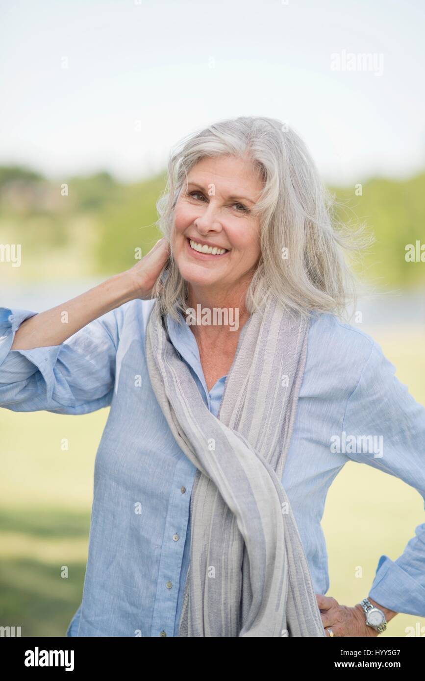 Senior donna con i capelli grigi e sciarpa all'aperto, sorridente. Foto Stock
