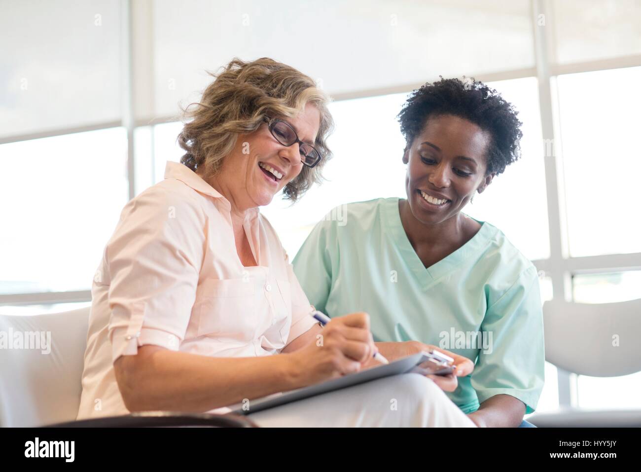 Donna matura la compilazione con l'infermiera, sorridente. Foto Stock