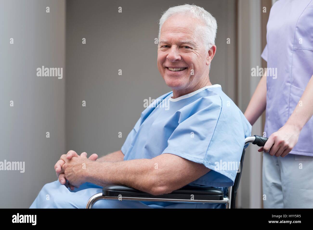 Senior uomo in abito ospedale in sedia a rotelle e sorridente. Foto Stock