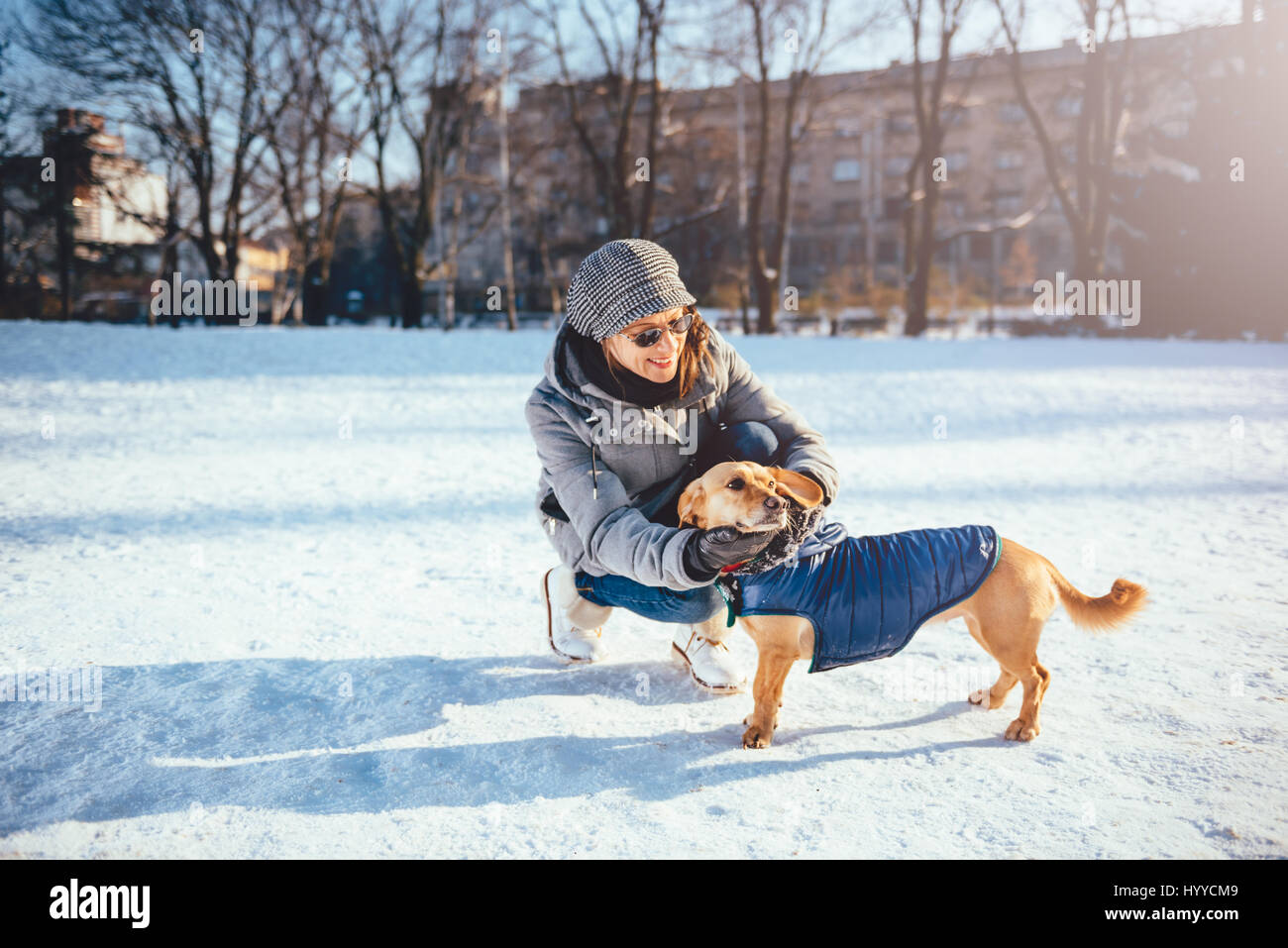 La donna come accarezzare il suo cane indossando cappotto invernale sulla neve Foto Stock