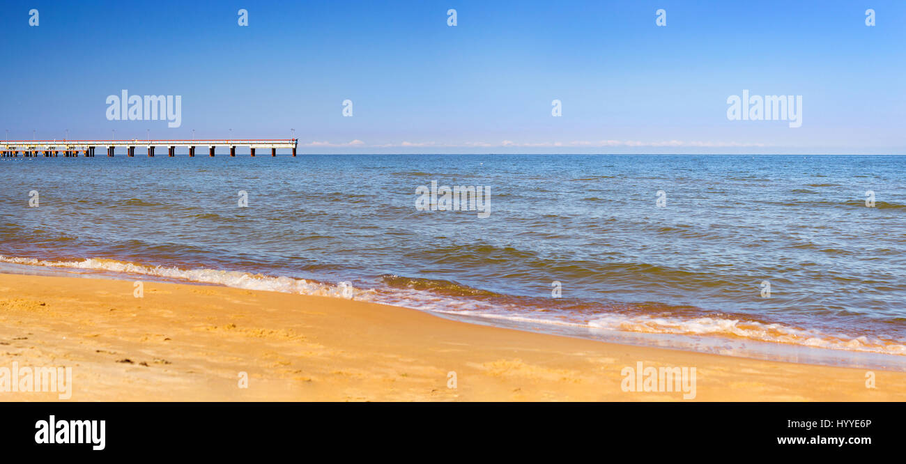 Caldo giorno d'estate sulla spiaggia sabbiosa dal Mar Baltico in lituano resort Palanga. Il molo pedonale si estende nel mare. Le onde di marea lavare la spiaggia sabbiosa Foto Stock