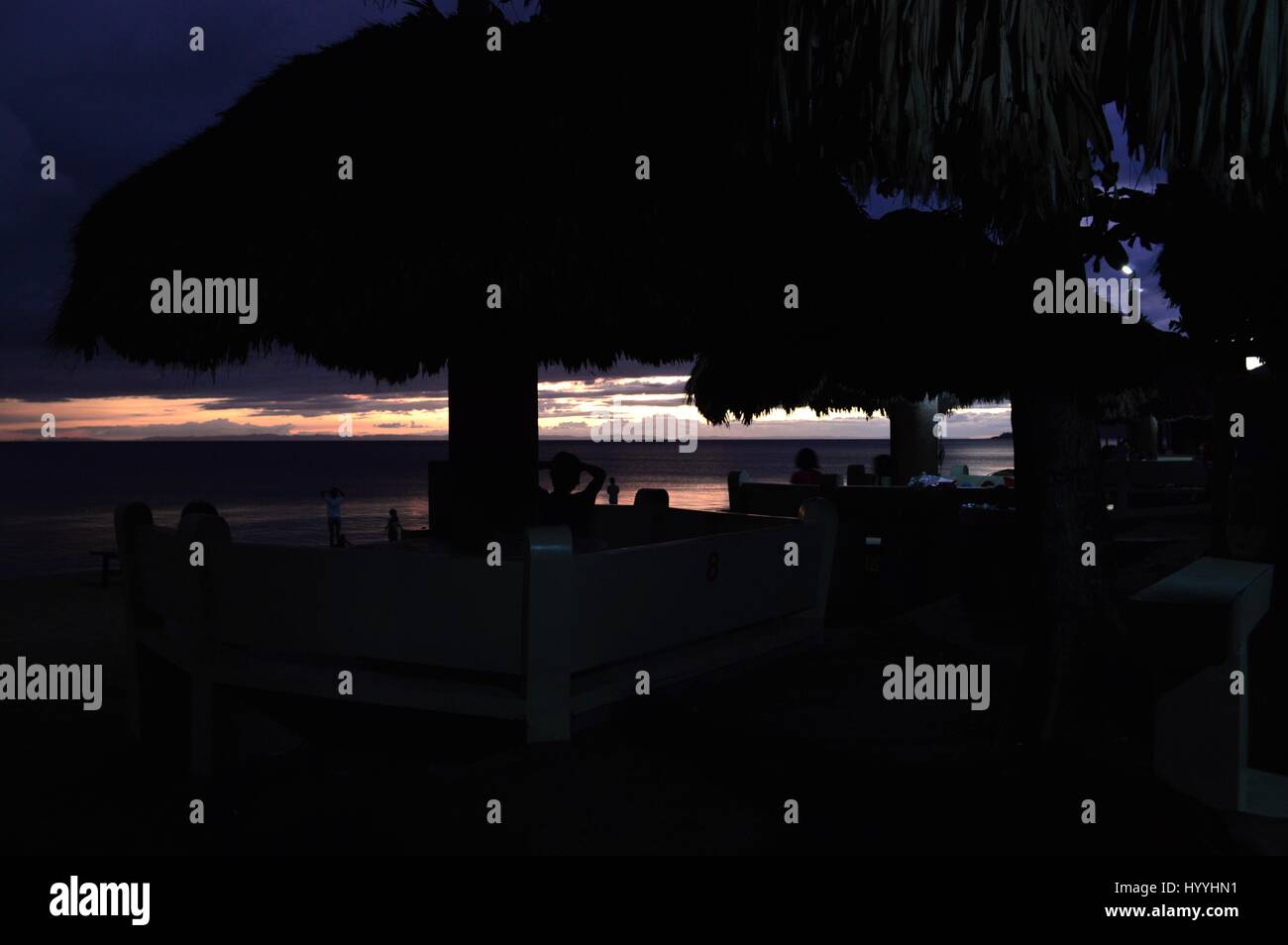 Silhouette di capanna post e baldacchini contro la spiaggia, il mare e il tramonto in background in un resort sulla spiaggia, Caranan Pasacao, Bicol, Filippine. Foto Stock