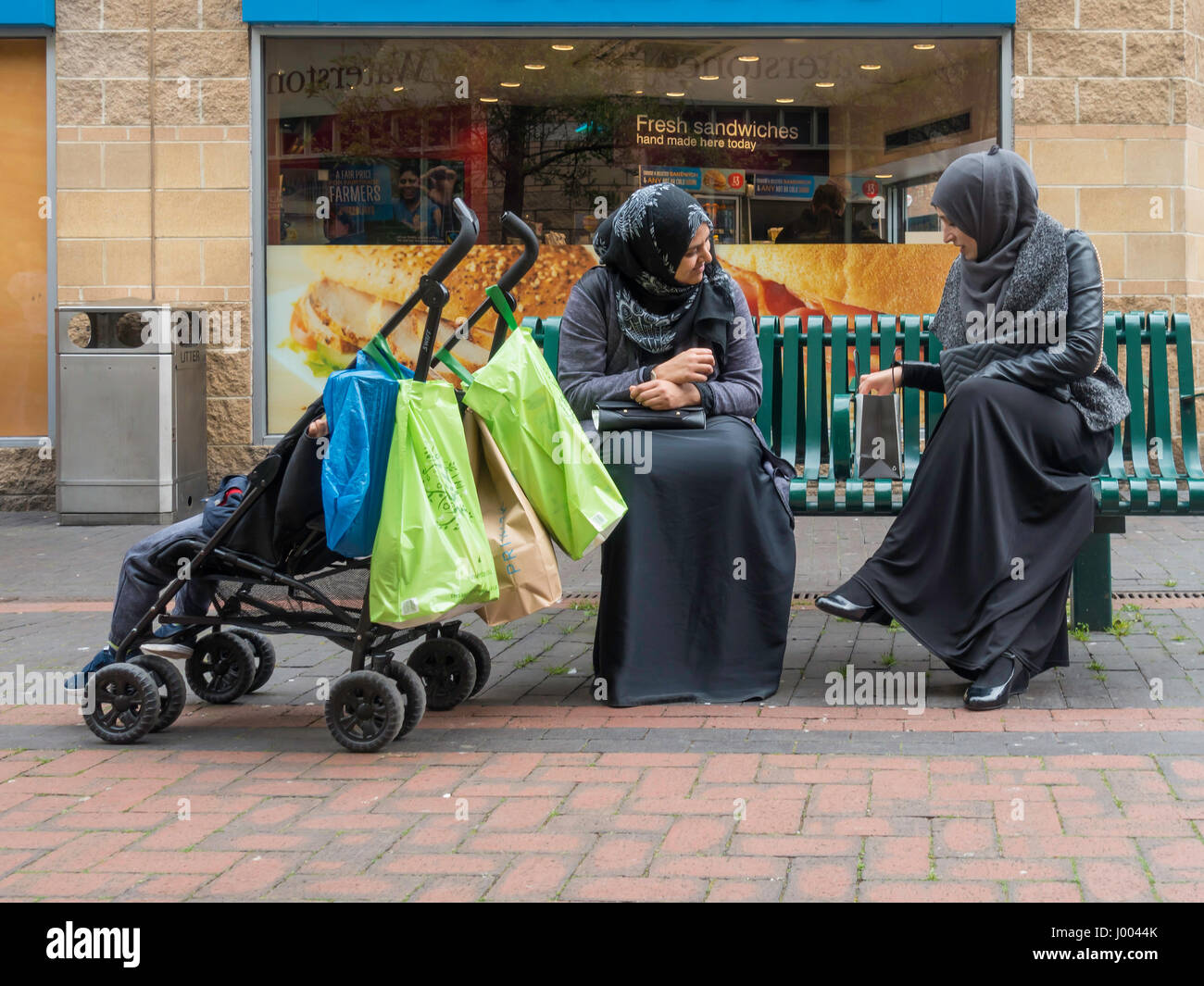 Due musulmani vestito ladies chiacchierare insieme in una sede pubblica moddlesbrough in centro città con un bambino in un bambino passeggino Foto Stock