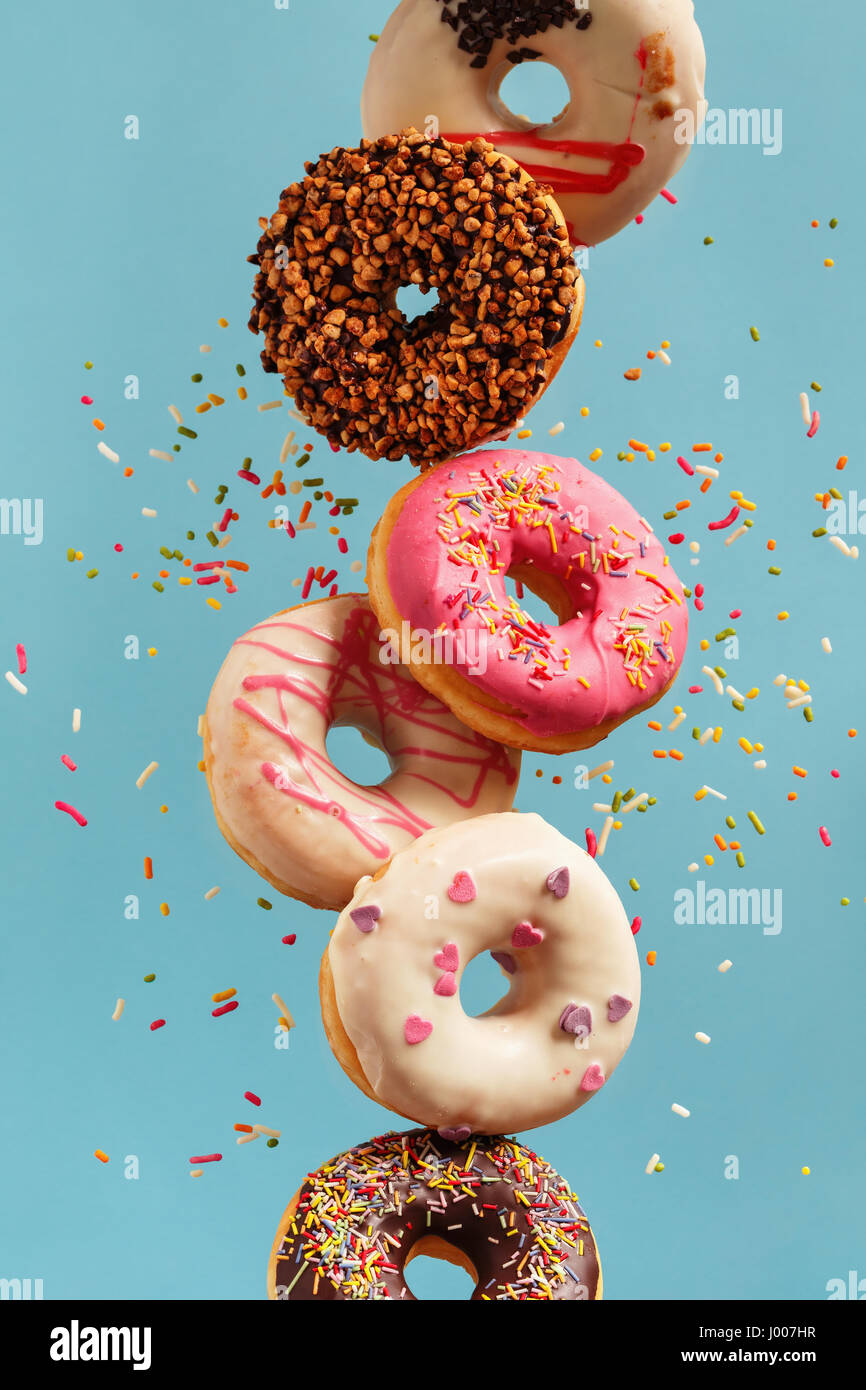 Varie ciambelle decorate in movimento che rientrano su sfondo blu. Dolce e colorata ciambelle di caduta o battenti in movimento. Foto Stock