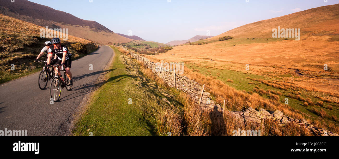 Due ciclisti salire uno stretto vicolo del paese attraverso la montagna paesaggio di brughiera del Newlands Valley vicino a Keswick in Inghilterra del Lake District. Foto Stock