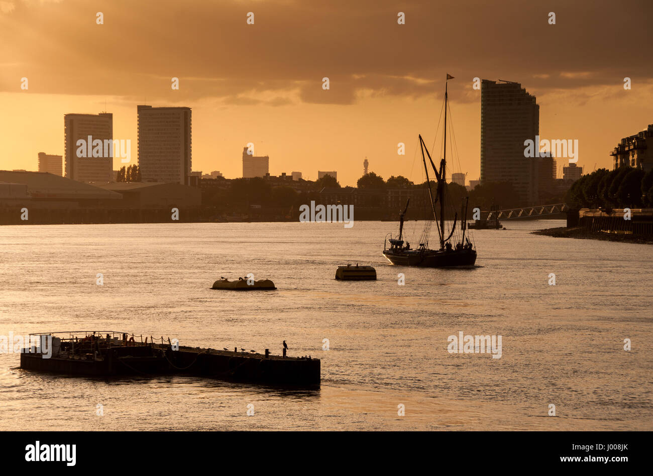 Tradizionale sul Fiume Tamigi chiatta a vela Barche si stagliano contro il tramonto a Greenwich, con edifici di appartamenti e ufficio blocchi dietro. Foto Stock