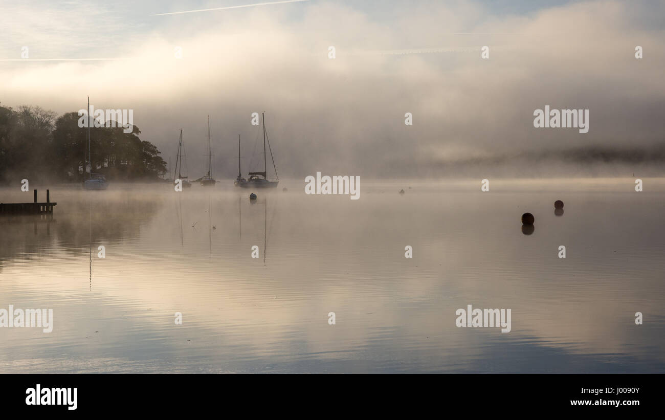 La nebbia sorge intorno alle barche ormeggiate sul lago di Windermere a Ambleside in Inghilterra del Parco Nazionale del Distretto dei Laghi. Foto Stock