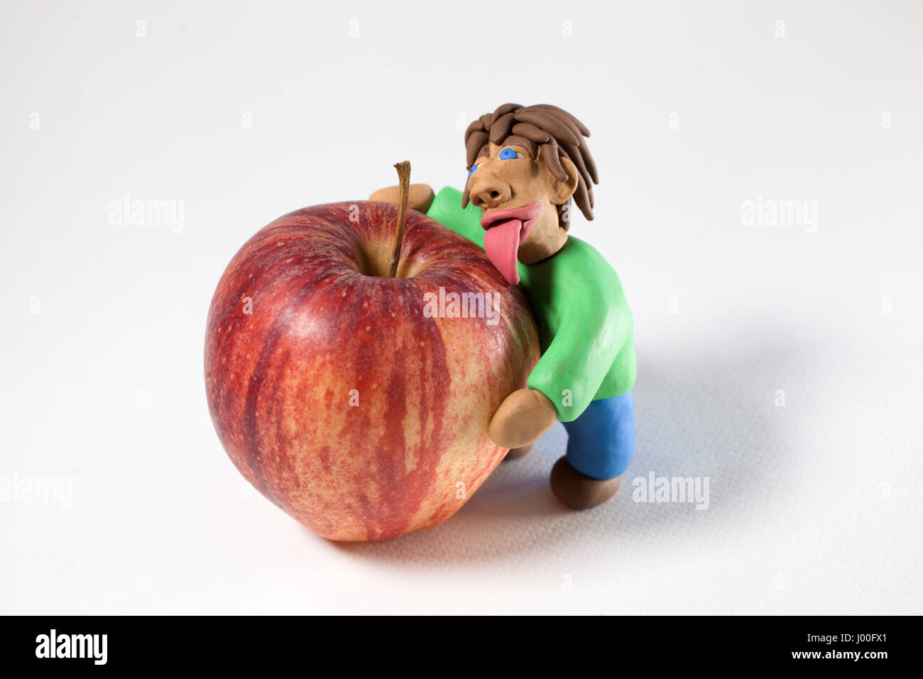 L'uomo fatto di creta per modellare leccare e abbracciando una mela rossa su uno sfondo bianco Foto Stock