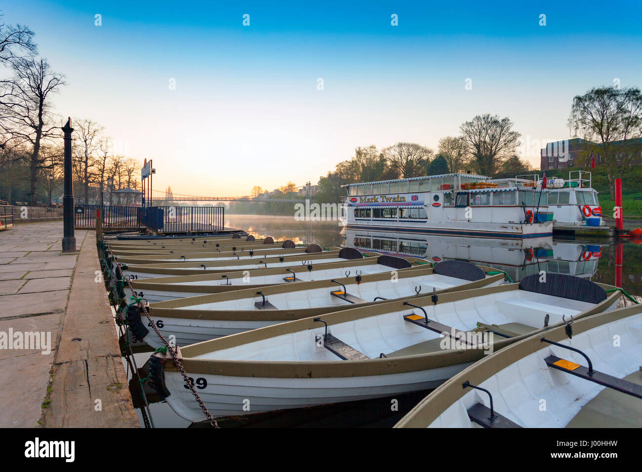 Barche ormeggiate fino contro la banca del fiume Dee all alba con tourist travel tour barche nel mezzo del fiume come il sole sorge e bagna il fiume in un caldo misty glow, Chester, England, Regno Unito Foto Stock