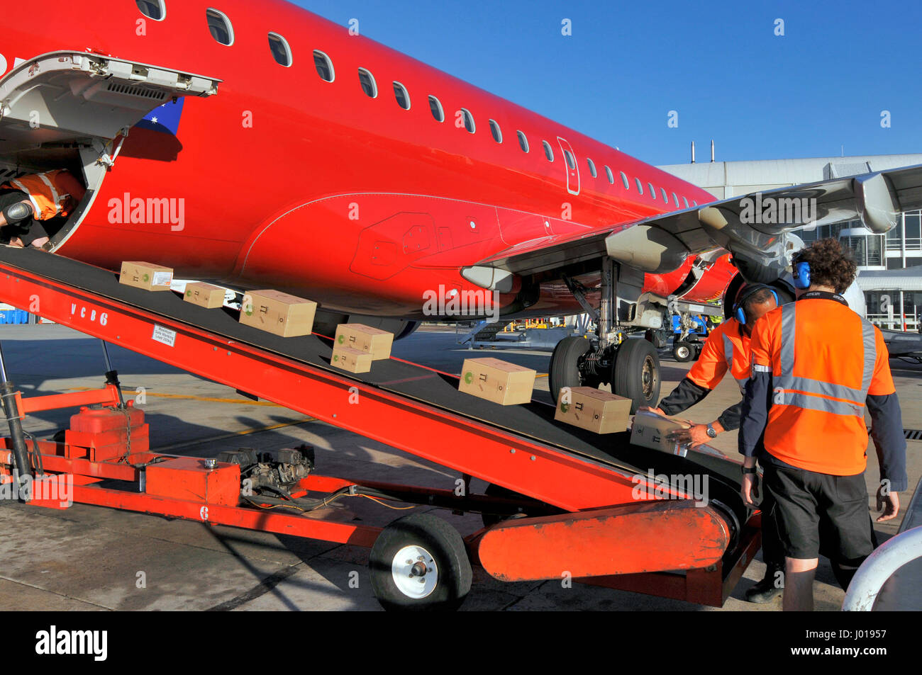 Lo scarico di merci da un red Embrarer EMB190 aereo di linea in un aeroporto. Foto Stock